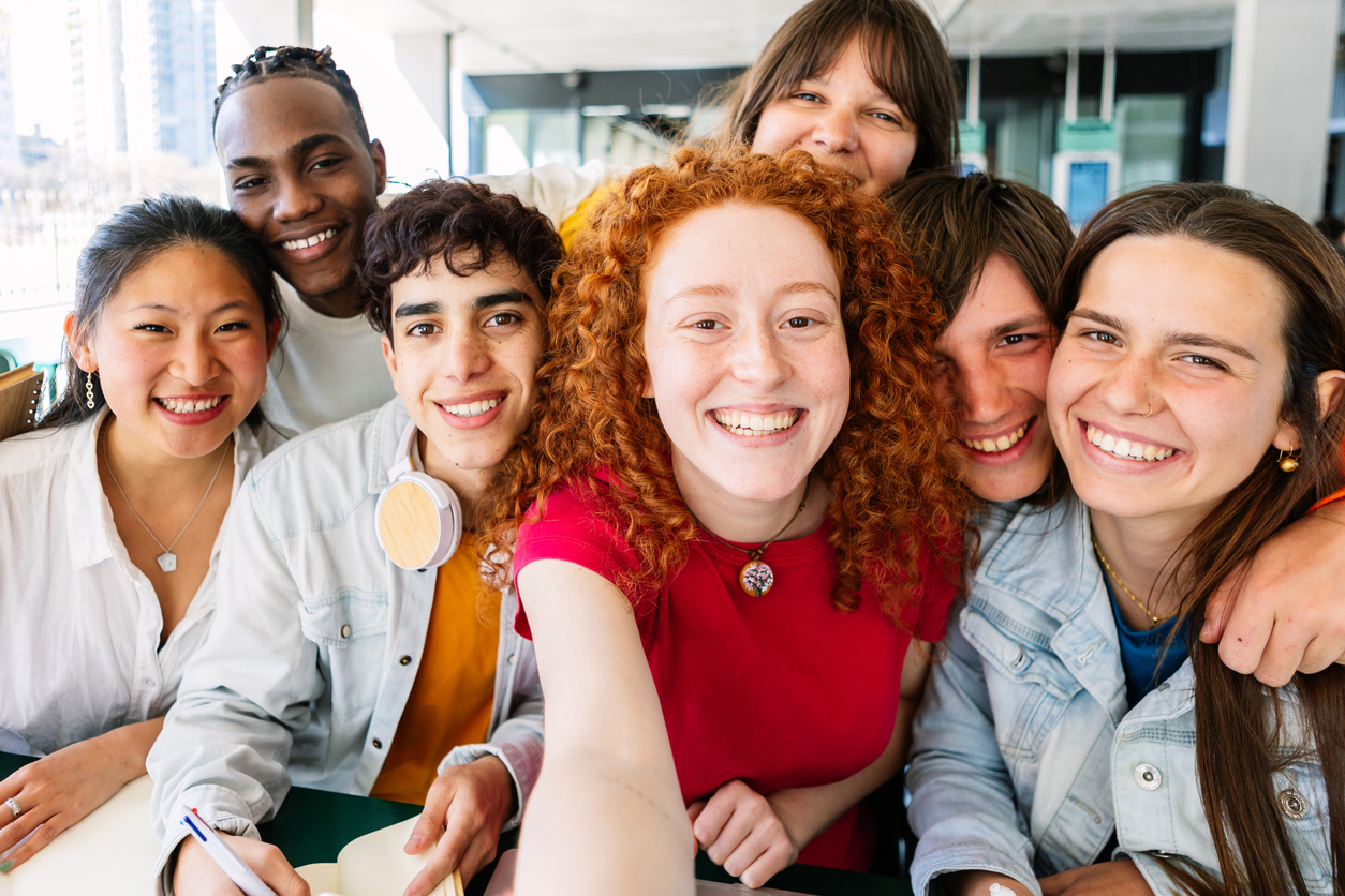 Multiracial group of young student people taking selfie while studying together sitting on table at cafeteria college campus.